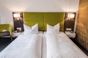 A hotel room with two single beds, a green upholstered headboard, bedside lamps, a desk with a telephone, and a chair. - Hotel Vorfelder (Walldorf)