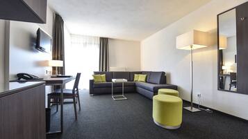 A modern hotel room with a desk, chair, sofa, and ottoman.