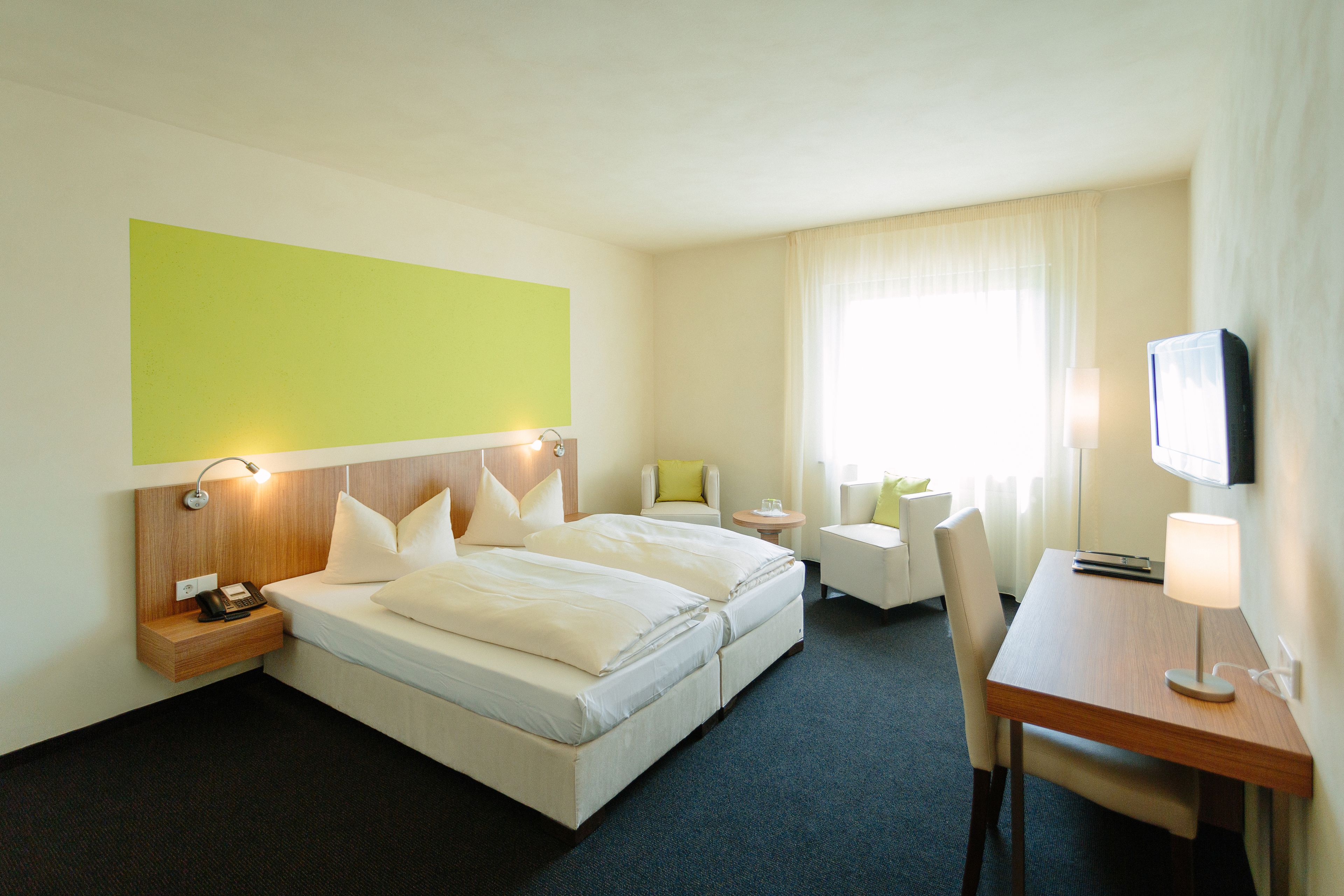 A hotel room with a bed, bedside table, chair, desk, and a television.