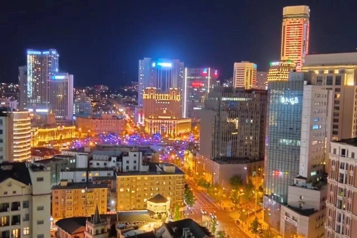 Une vue nocturne d’une ville, avec des bâtiments illuminés et une rue animée.