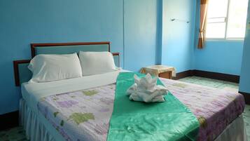 Una cama bien hecha con sábanas blancas y una colcha de estampado floral. Hay una toalla verde sobre la cama y un pequeño taburete de madera a su lado.