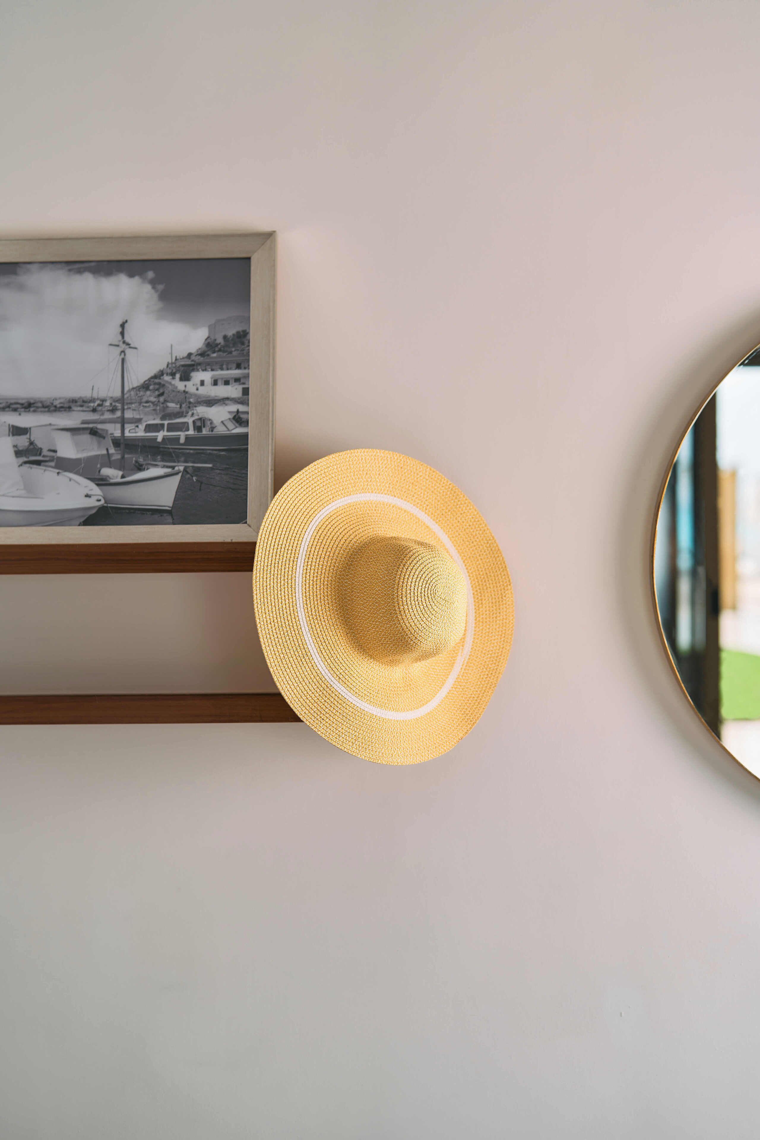 Fotografia in bianco e nero incorniciata, raffigurante una scena costiera con barche, un cappello e uno specchio rotondo appeso a una parete.