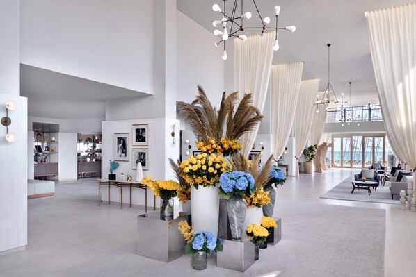 A spacious lobby with a modern design, featuring a central floral arrangement, a seating area, and a view of the ocean through large windows. - Al Alamein Hotel (El Alamein)