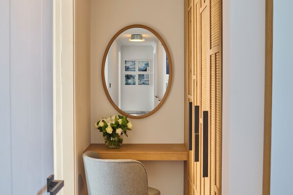 Une pièce avec un miroir, une étagère en bois ornée d’un vase de fleurs et une porte donnant sur l’extérieur.