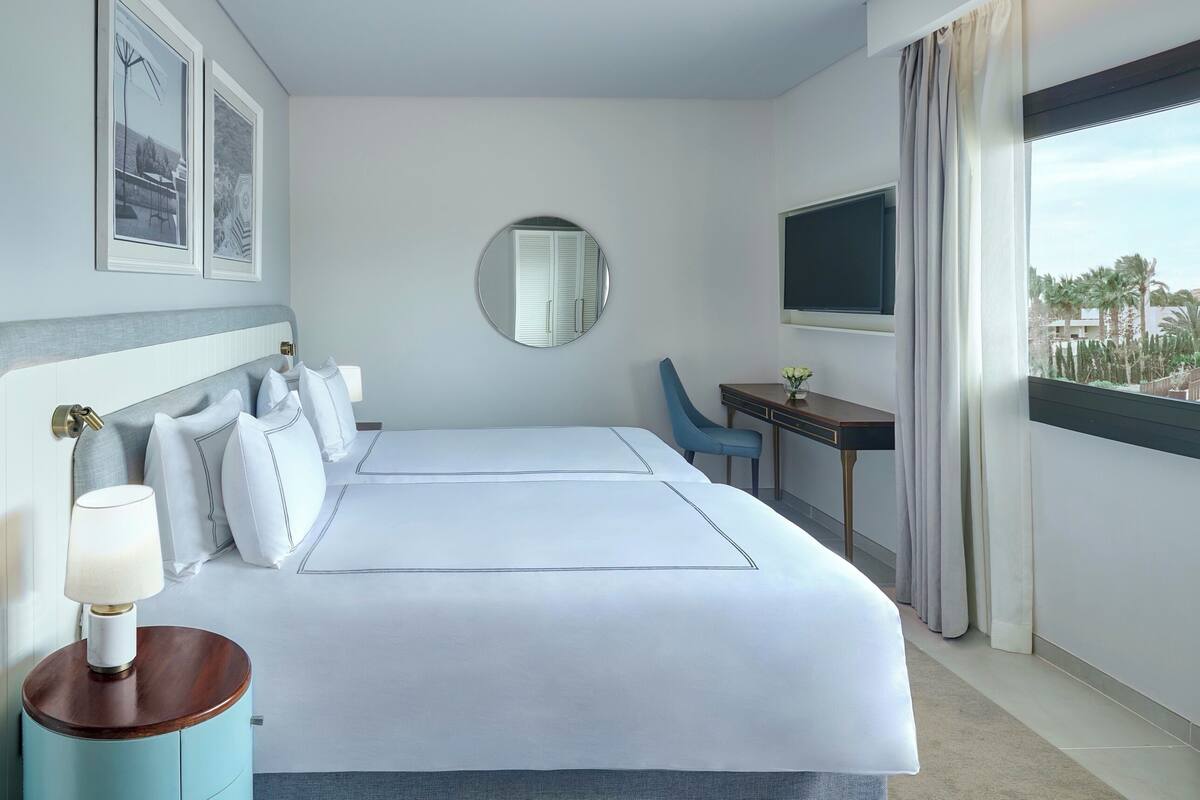 A hotel room with a large bed, a desk, a chair, a TV, a mirror, and framed pictures on the wall.