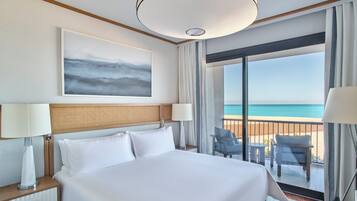 A hotel room with a bed, two bedside lamps, a large window with a view of the beach, and a ceiling light.