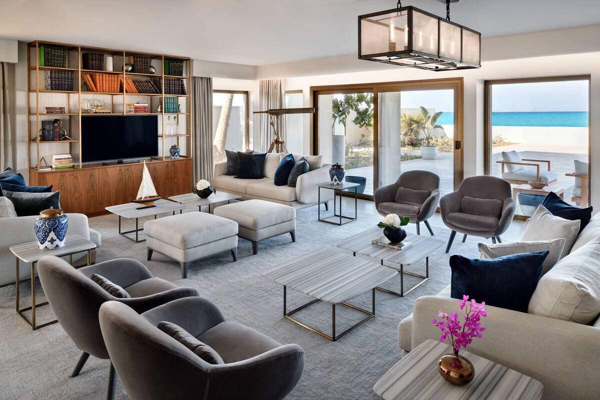 A spacious living room with a large bookshelf, a flat-screen TV, and a view of the beach.