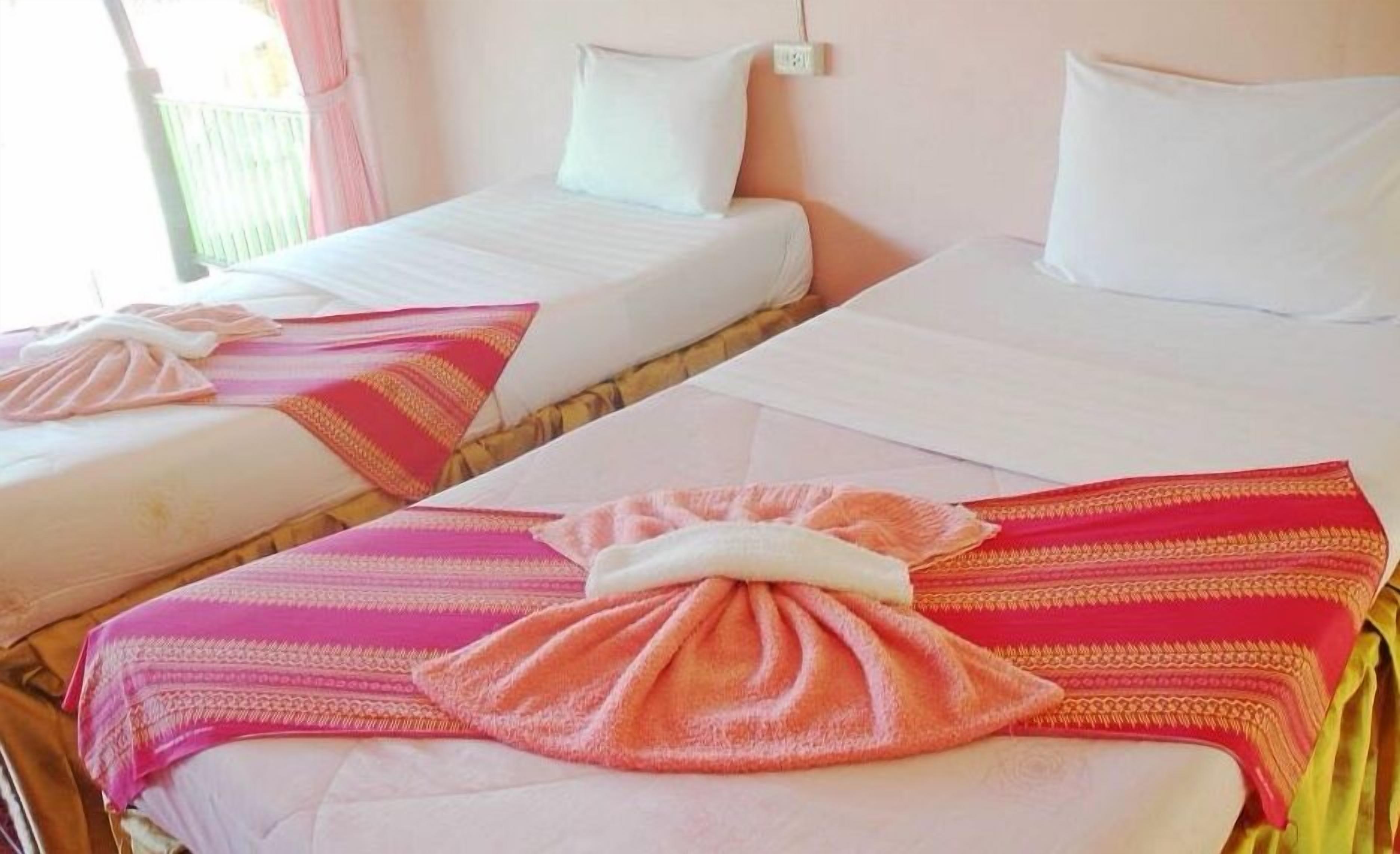 Two single beds with white linens and pink and red patterned blankets.