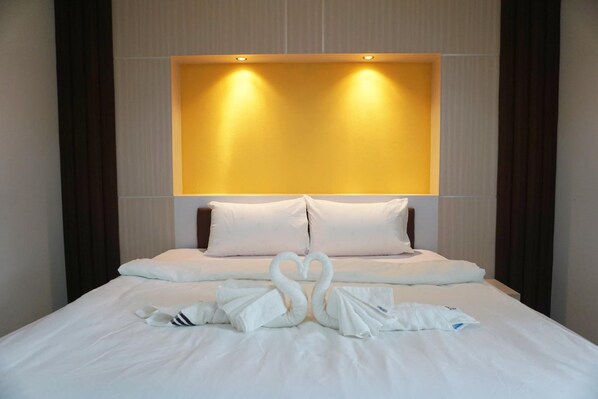 Quarto de hotel com uma cama grande, roupa de cama branca, cabeceira com iluminação integrada e um arranjo de toalhas em forma de cisne sobre a cama.