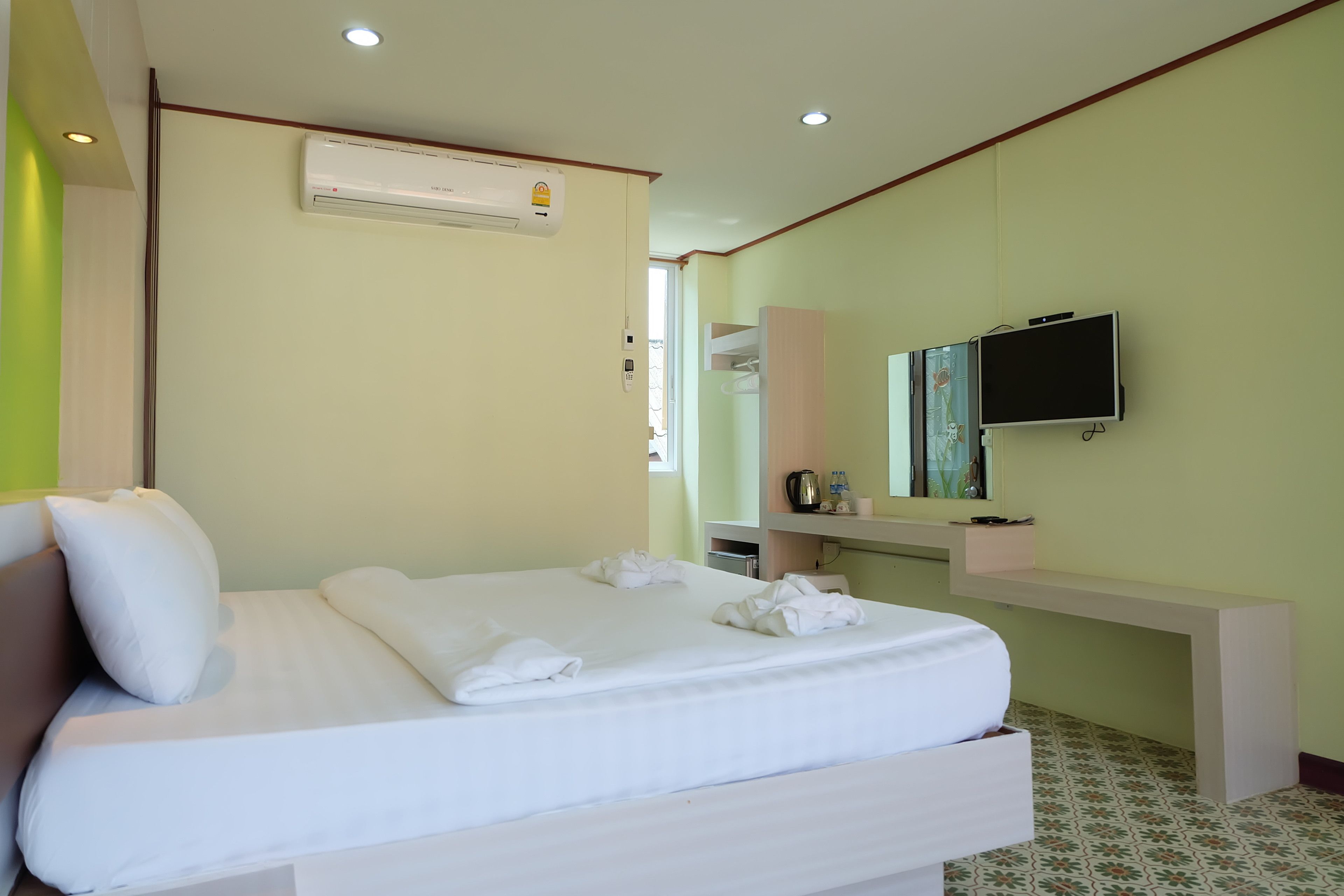A hotel room with a bed, a TV, a desk, and an air conditioning unit.