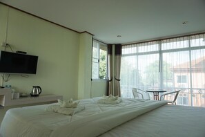Quarto de hotel com uma cama grande, televisão na parede, uma mesinha com cadeiras e uma varanda com vista para o exterior.