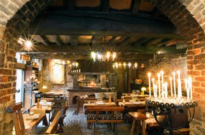 A cozy restaurant with brick walls, exposed beams, and a central fireplace. Tables are set with candles and tableware. - Auberge Du Bon Fermier (Valenciennes)