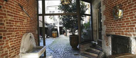 A cobblestone courtyard with a stone bench, a large planter, and a wooden door.
