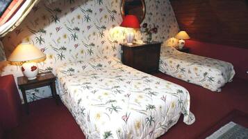 A bedroom with two beds, floral-patterned bedding, two bedside lamps, a mirror, and a small table with a vase.