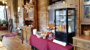 A rustic interior with a wooden counter displaying various items, a glass display case with bottles, and a red tablecloth-covered table with food and drinks. - Auberge Du Bon Fermier (Valenciennes)