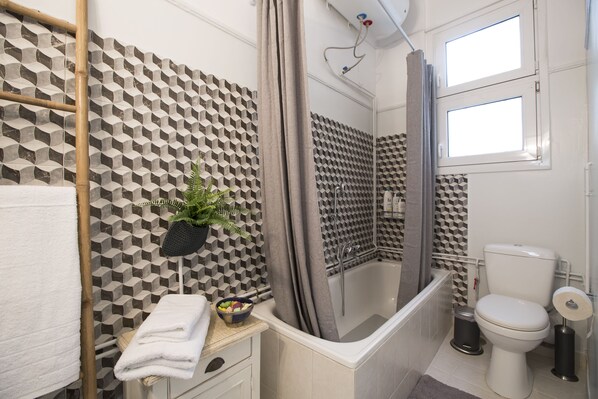 Un baño moderno con un revestimiento de pared de diseño geométrico, una bañera, un inodoro y un cubo de basura pequeño.