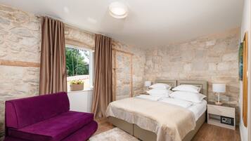 Ein Schlafzimmer mit Steinwand, einem Bett mit weißer Bettwäsche, einem violetten Sofa und einem kleinen Nachttisch mit Lampe.