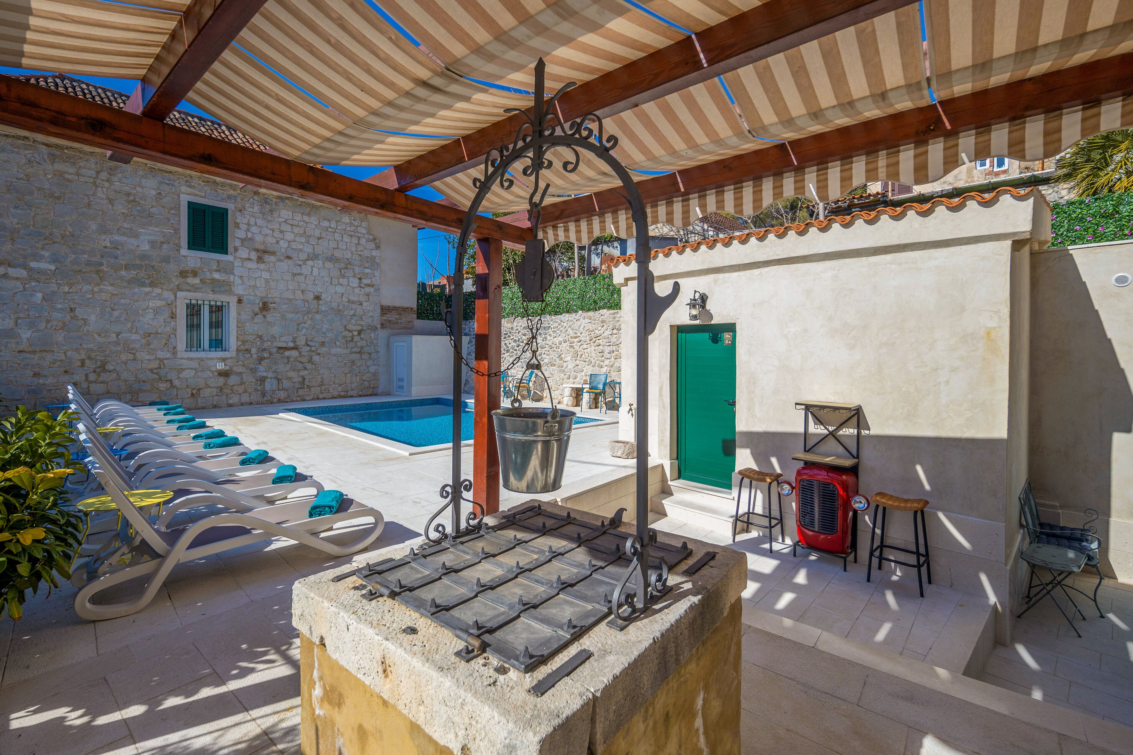 A poolside area with lounge chairs, a stone wall, a green door, and a red heater.