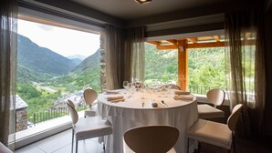 Mesa redonda para seis personas con sillas, ventanas grandes con cortinas y vista a un paisaje montañoso.