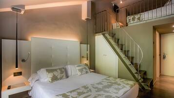 A bedroom with a bed, a nightstand, a lamp, a staircase, and a door.