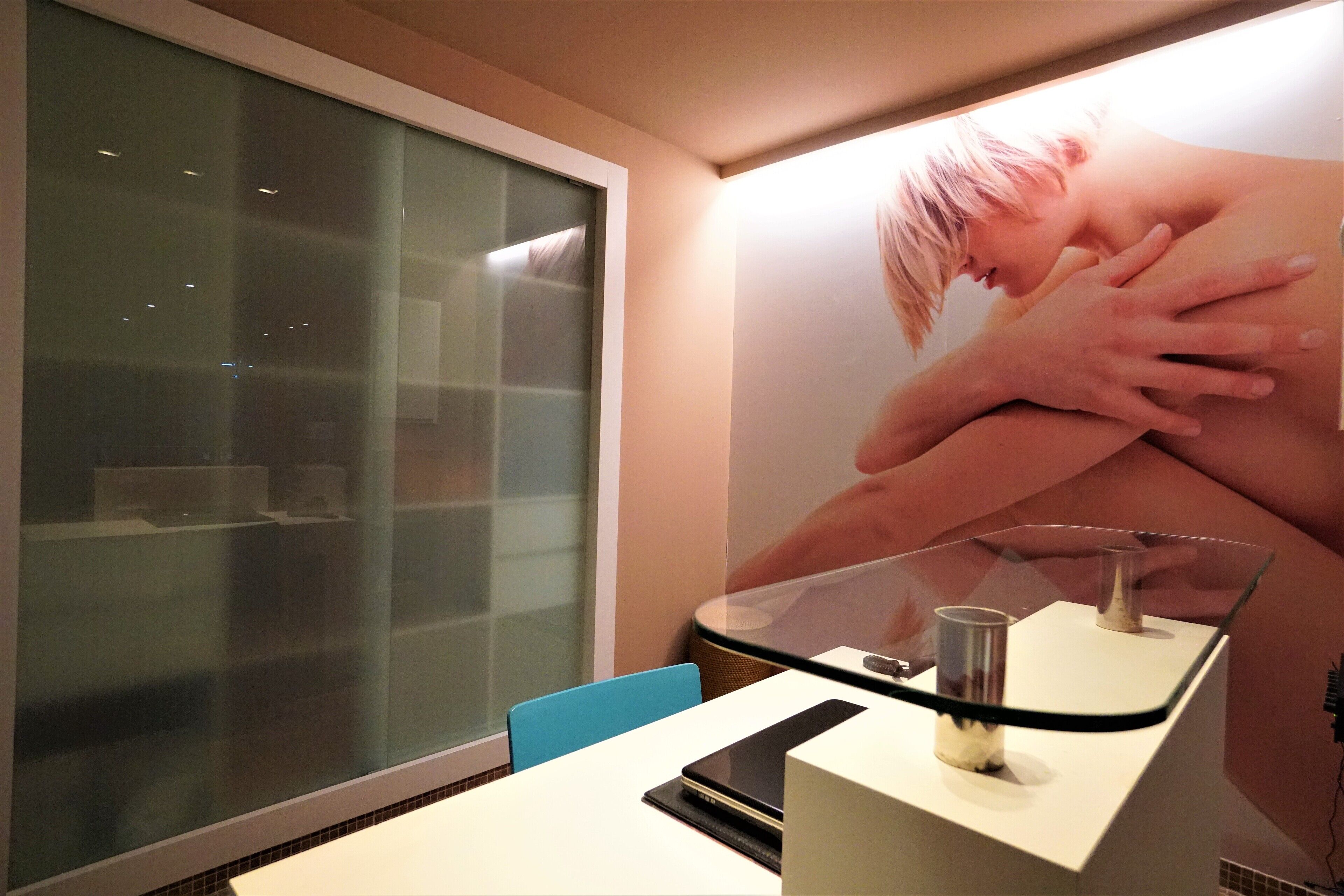 A modern room with a glass partition, a white desk, and a large poster on the wall.