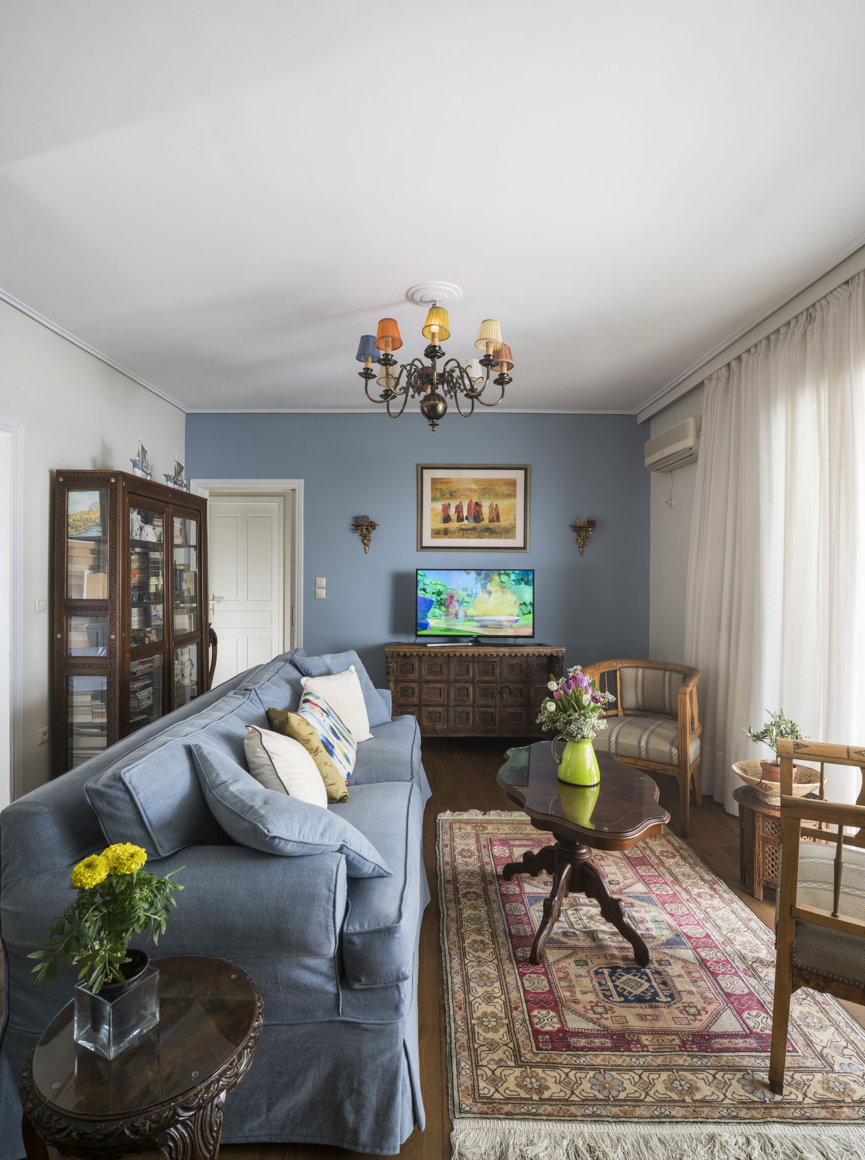 Ein Wohnzimmer mit einem blauen Sofa, einem Holzschrank, einem Fernseher und einer Chandelüster.