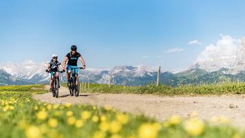 Dos ciclistas en un sendero de tierra con montañas al fondo.