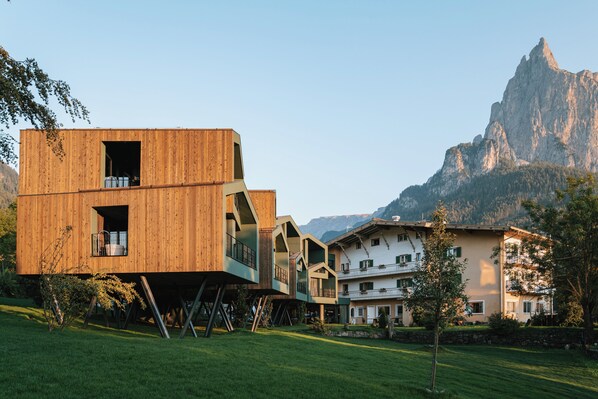 Un edificio moderno de madera con balcones, un paisaje montañoso al fondo y un césped bien cuidado.