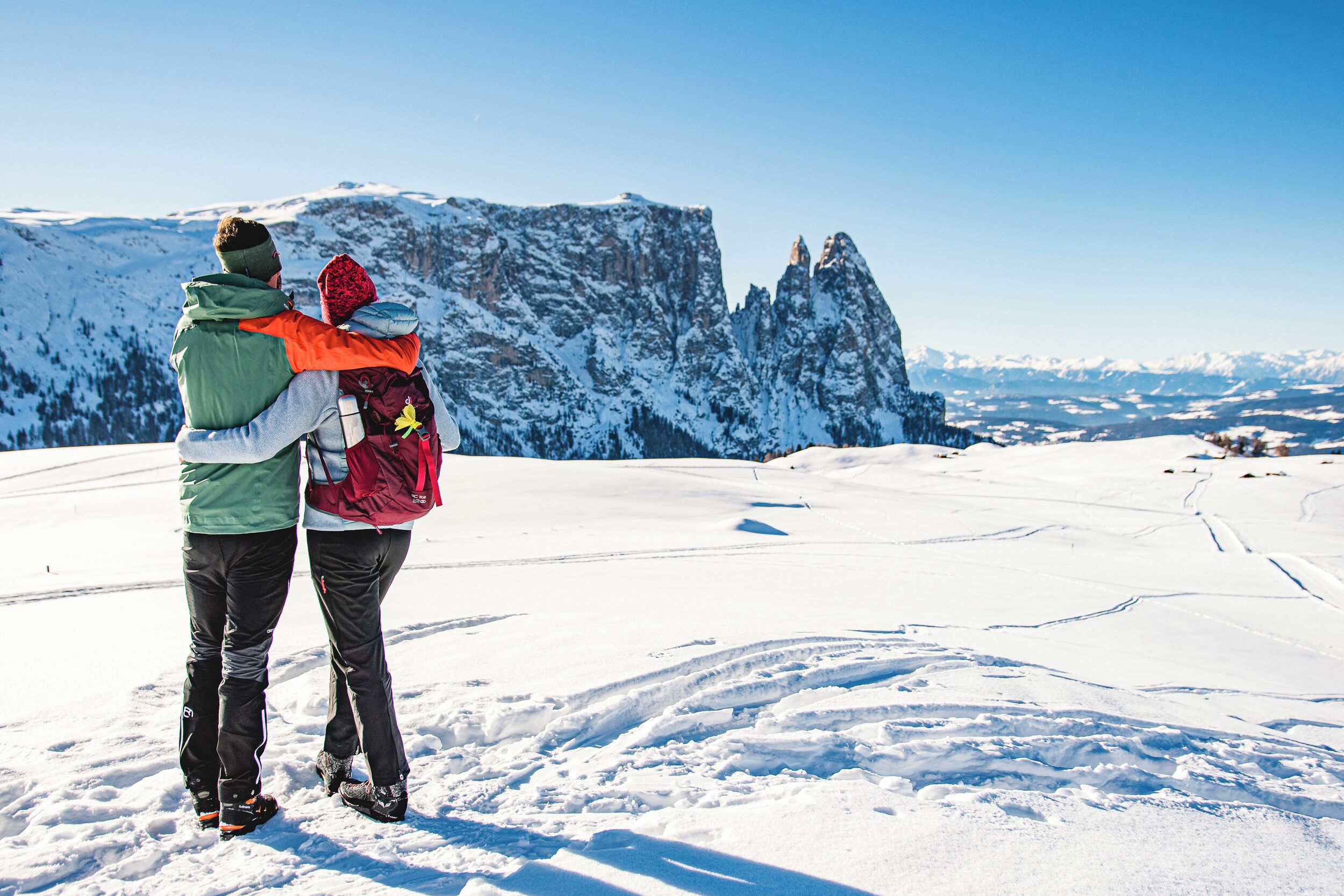 Una coppia in piedi su una montagna innevata con cielo sereno e vista sulle cime innevate.
