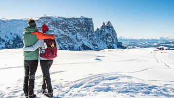 Una coppia in piedi su una montagna innevata con cielo sereno e vista sulle cime innevate.
