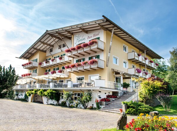 Ein Hotel mit mehreren Balkonen, die mit Blumen geschmückt sind, einem überdachten Außenbereich zum Sitzen und einer Steintreppe zum Eingang.