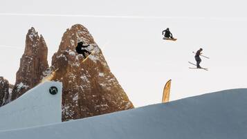 A ski slope with skiers performing jumps and a mountain backdrop.