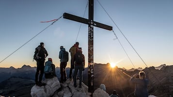 Un grup de persones al cim d'una muntanya amb una estructura de creu, en un paisatge rocosos i amb vistes al capvespre.