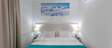 A hotel room with a bed, two bedside lamps, a headboard with a painting, and a window with curtains.