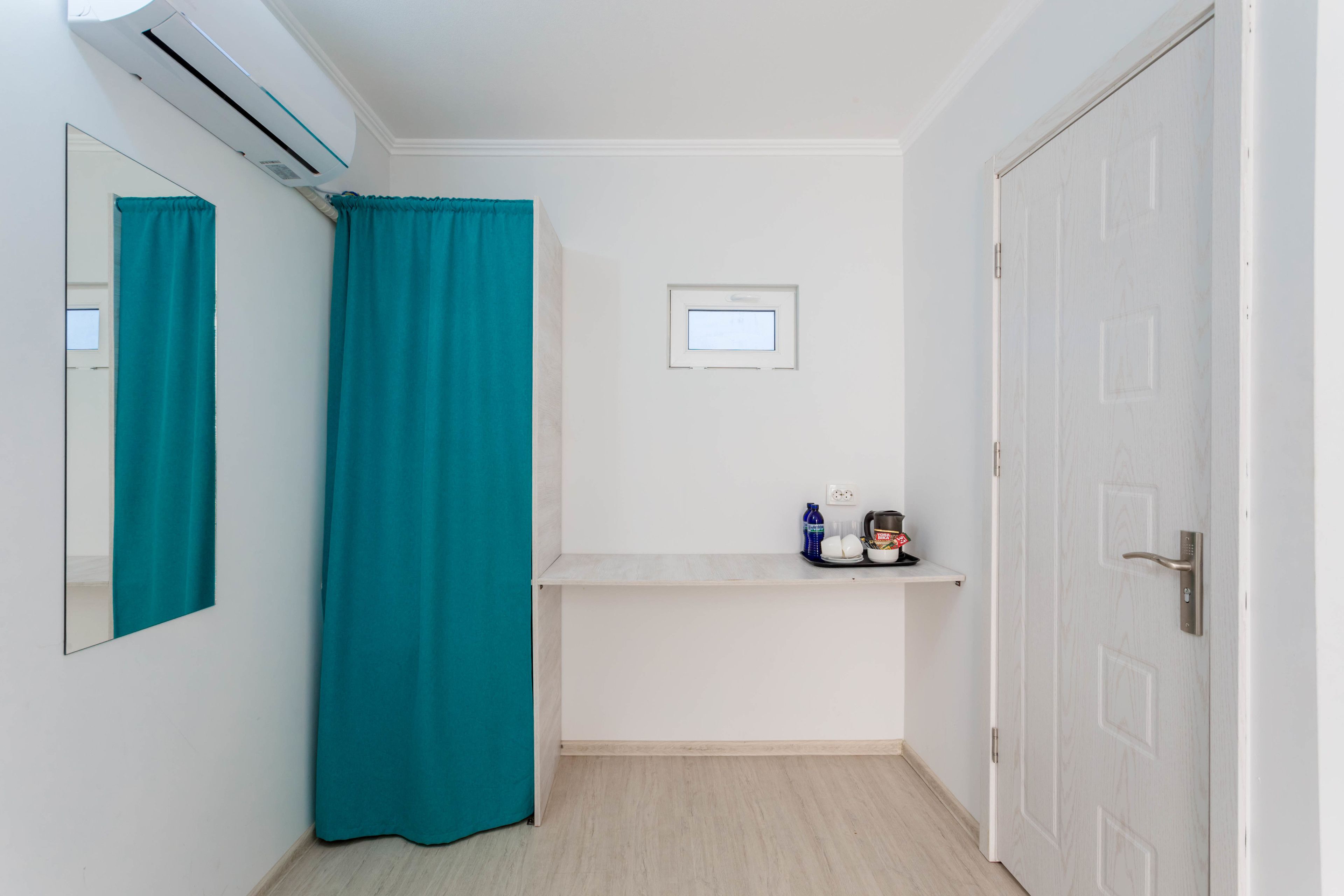 A small, clean bathroom with a teal shower curtain, a white sink with a mirror, and a door with a handle.