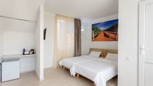 A bedroom with a bed, a desk, a small fridge, and a wall-mounted picture. - Hotel TATO (Tbilisi)