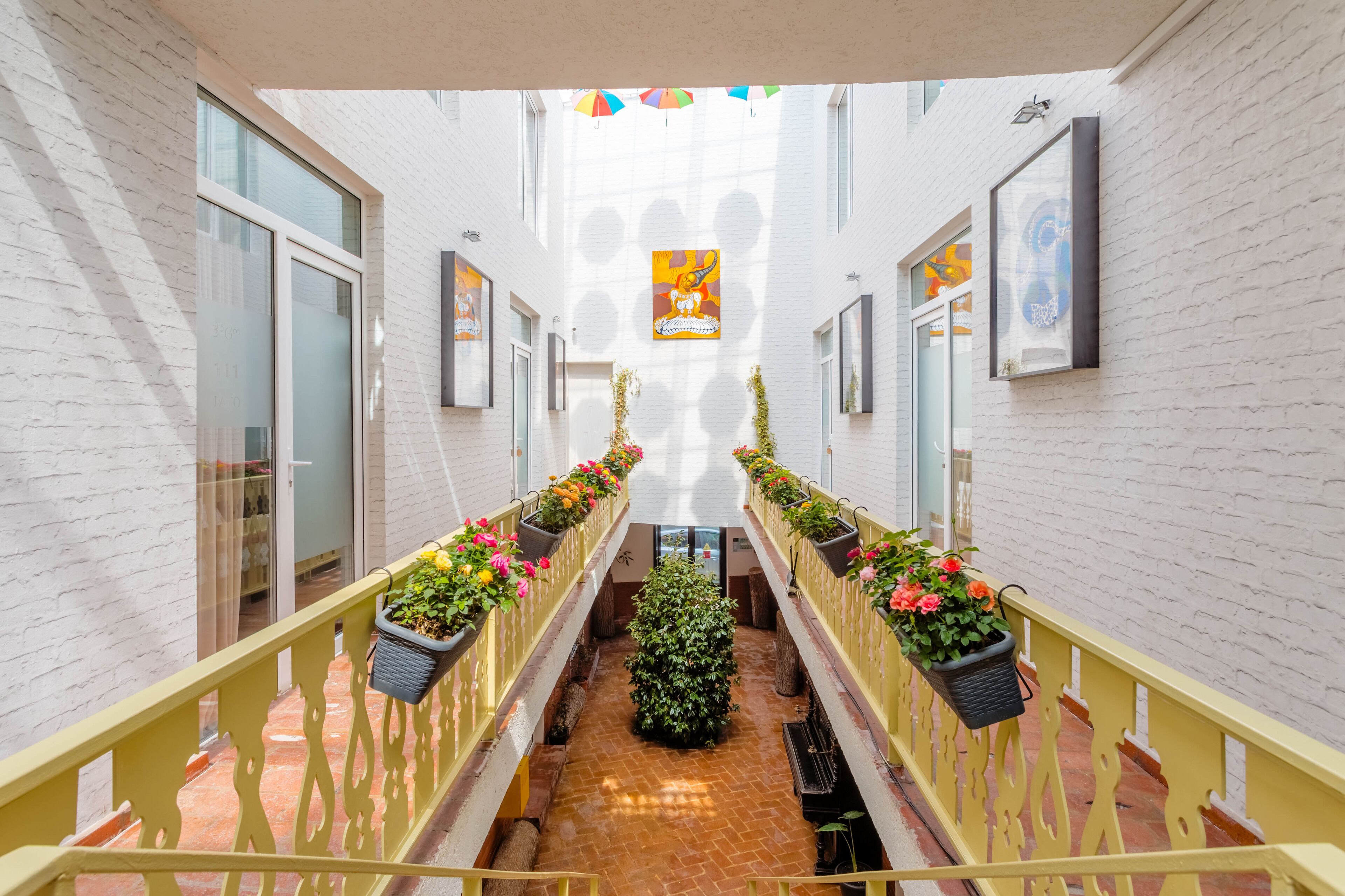 A corridor with white brick walls, yellow railings, and potted plants.