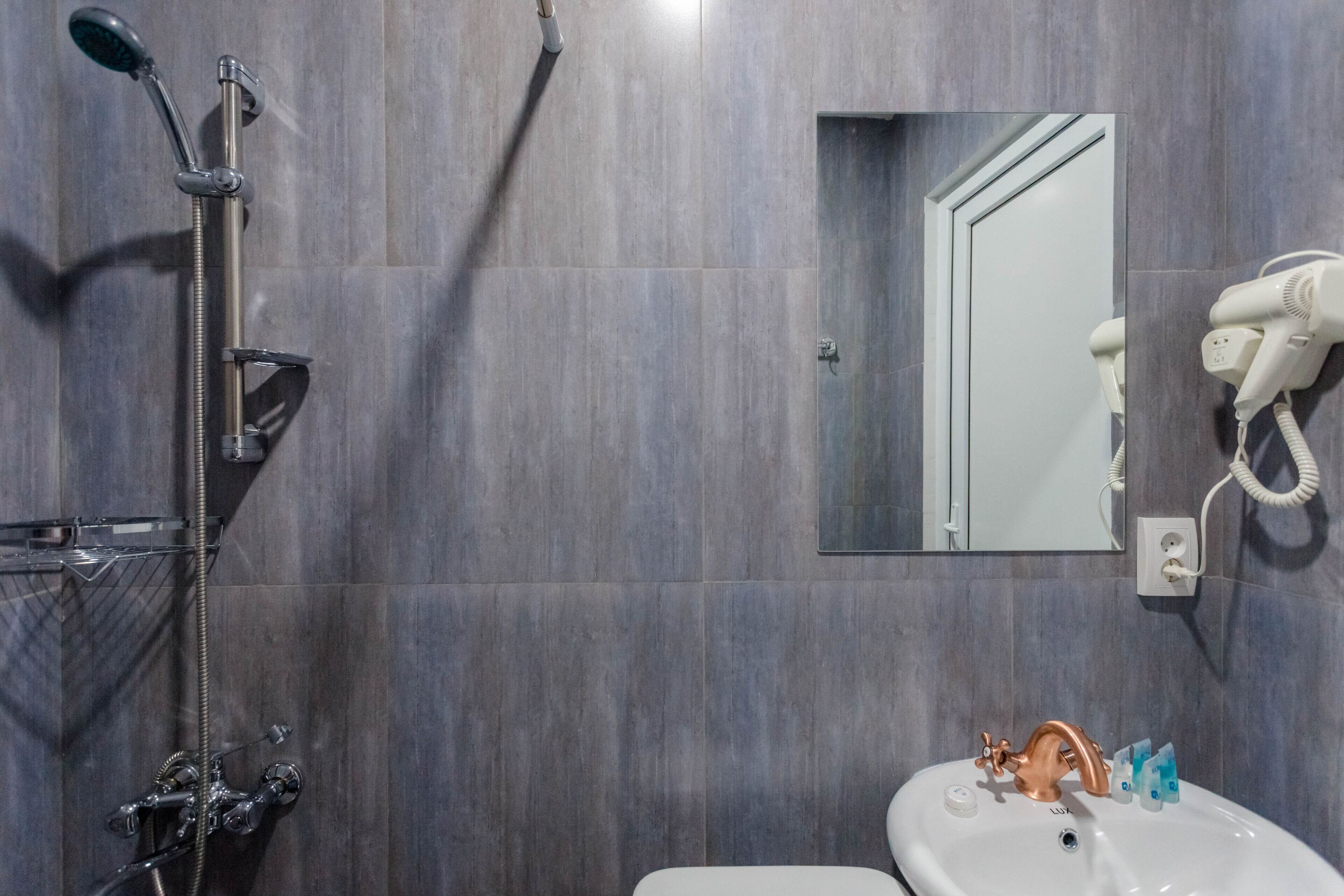 A modern bathroom with a shower, a sink, and a hairdryer mounted on the wall.
