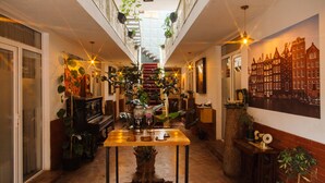 A narrow hallway with a staircase, a piano, a table with plants, and a cityscape mural. - Hotel TATO (Tbilisi)