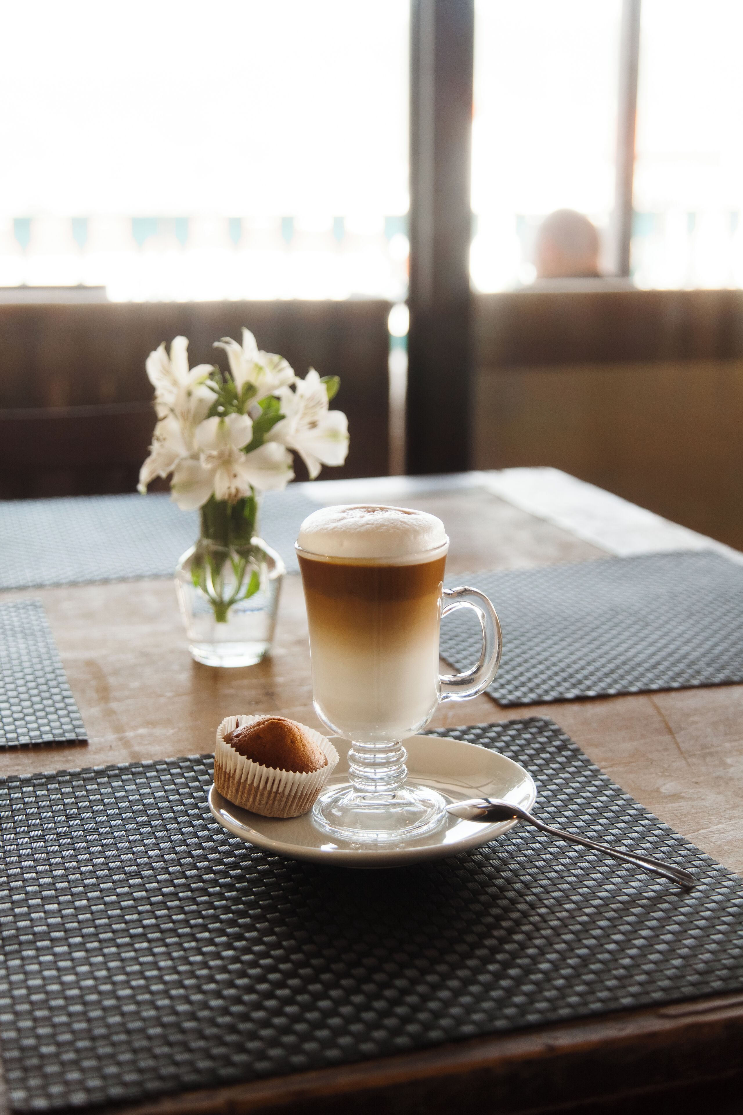A cup of coffee on a table with a muffin and a glass of water.
