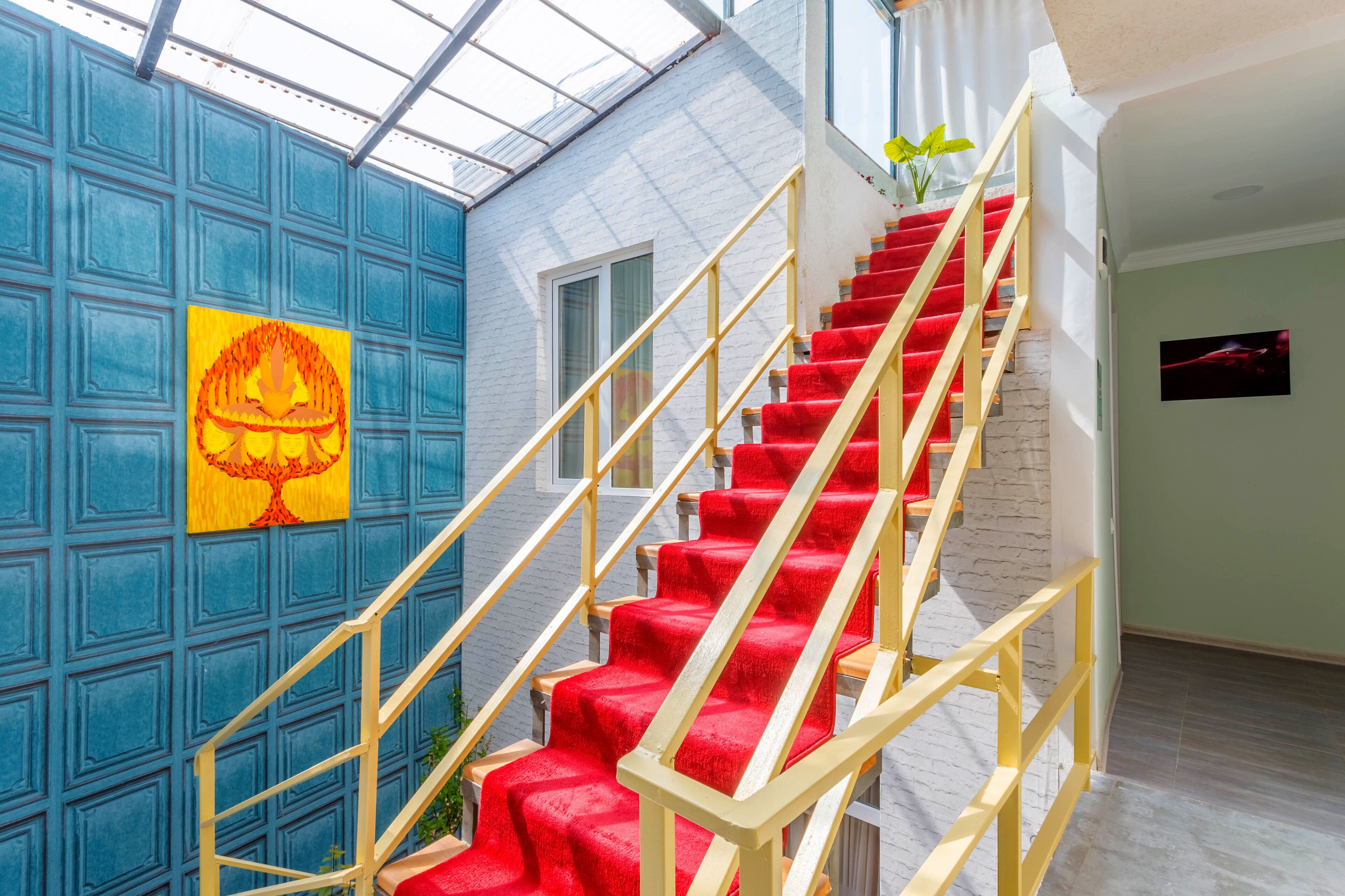 Eine Treppe mit roten Teppichstufen und geländer, die zu einem Raum mit weißer Backsteinwand und einem Fenster führt.