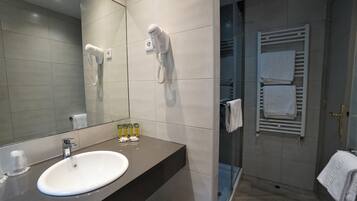 Un baño moderno con un lavabo blanco, un secador de pelo fijado a la pared y un box de ducha de cristal.