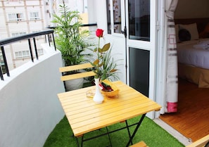 Un balcón con una mesa de madera, una planta en maceta y una rosa roja.