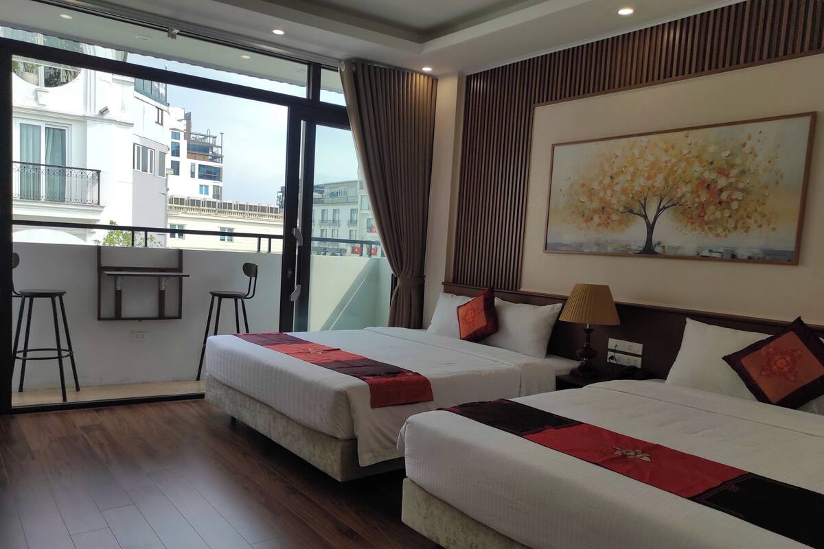 Une chambre d’hôtel avec deux lits, un balcon avec une chaise, une petite table et un tableau au mur.