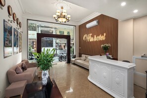 Uma área de recepção de hotel com balcão, sofá, planta em vaso e lustre.