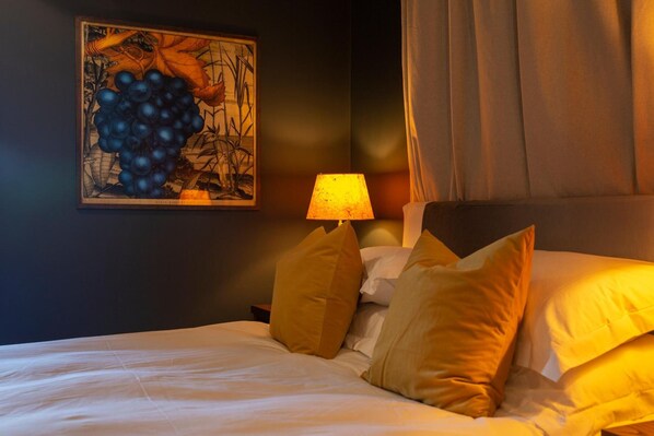 A neatly made bed with a headboard, a bedside lamp, and a wall-mounted painting. - The Princess Victoria (London)