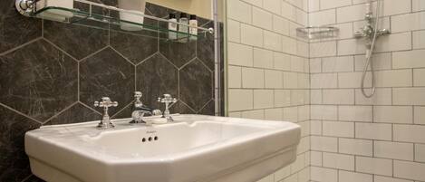 A bathroom with a white sink, dark marble backsplash, and a glass shower enclosure.