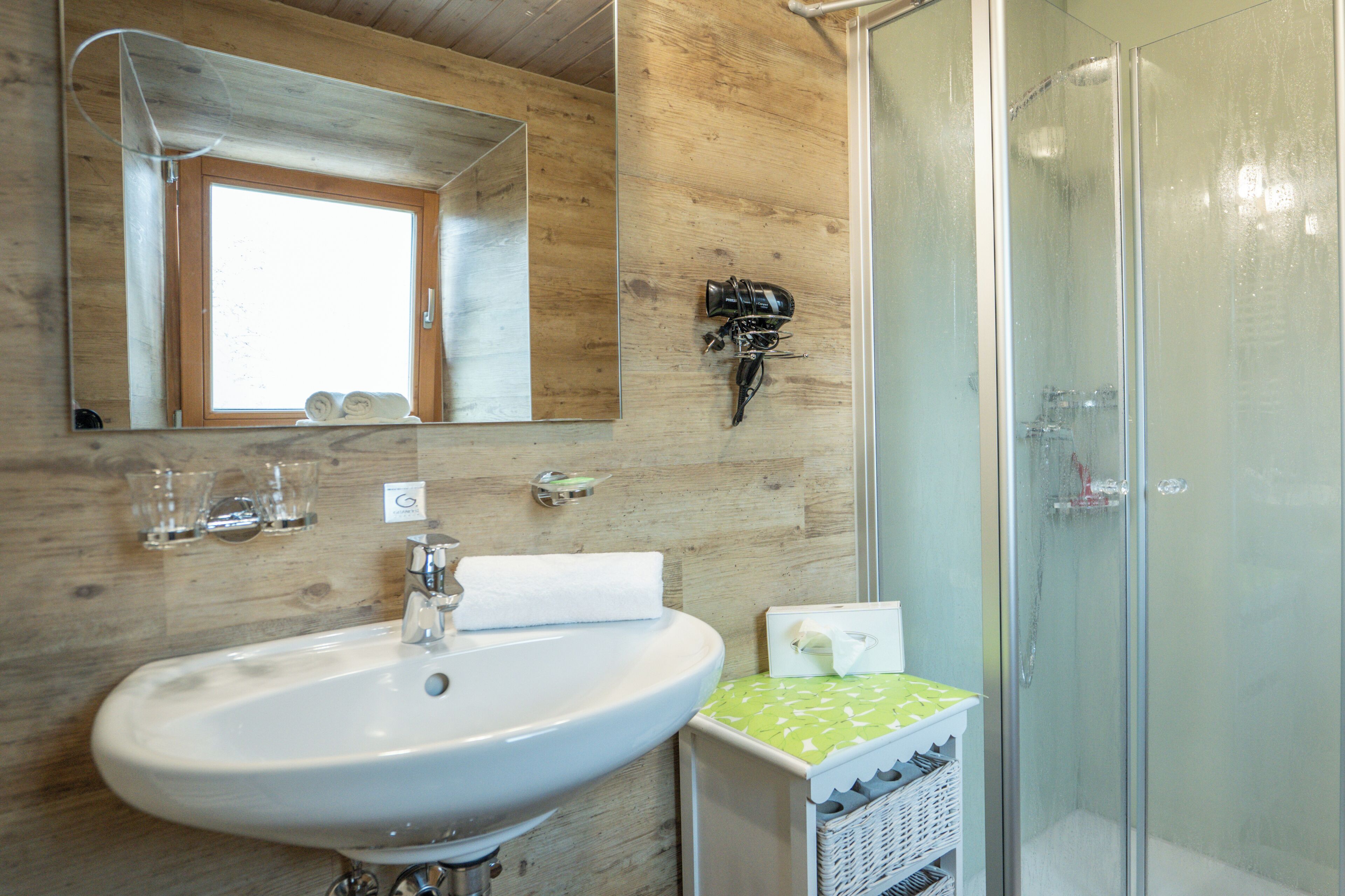 A bathroom with a wooden wall, a sink, a mirror, a shower, and a towel rack.