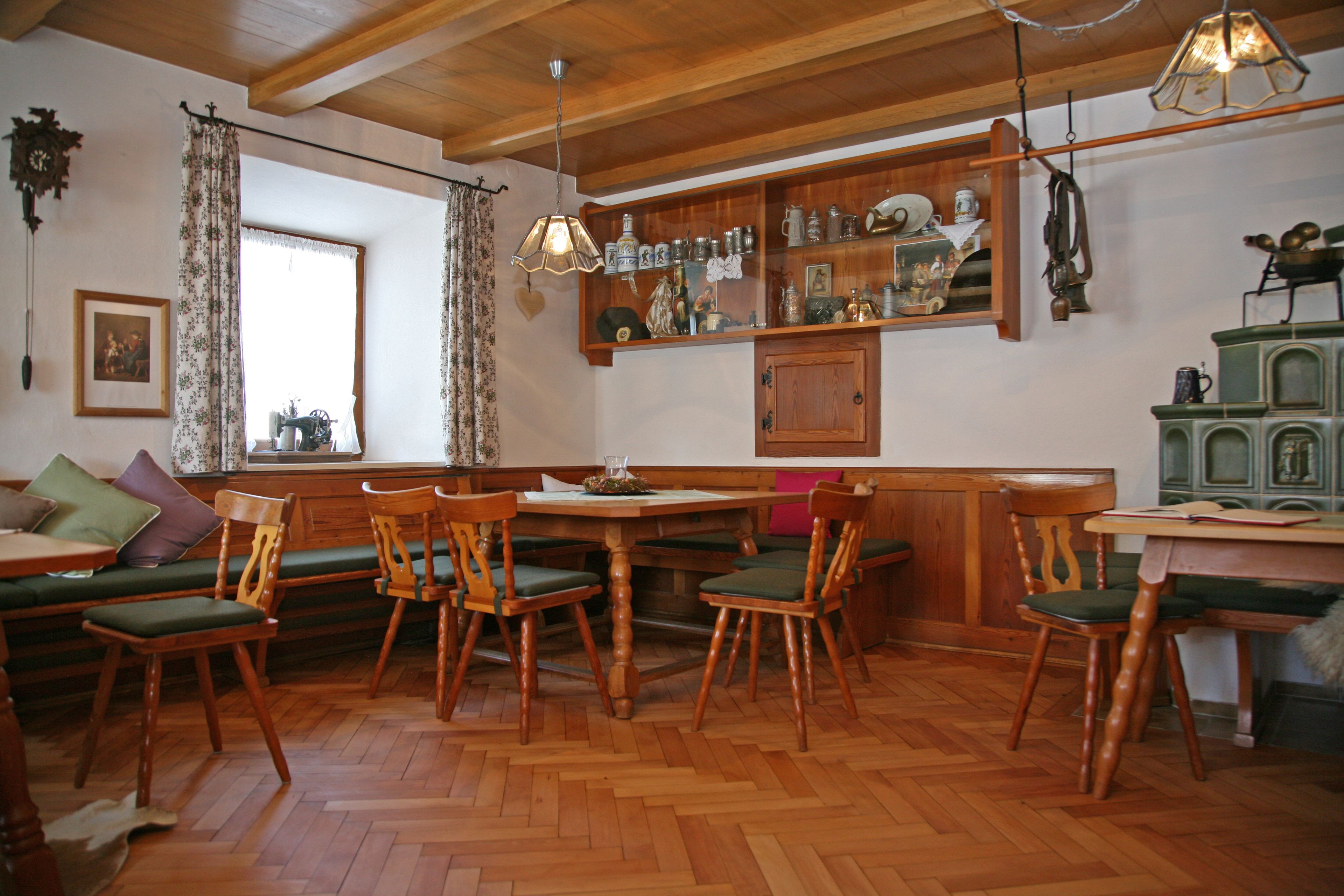 A wooden dining area with a herringbone floor, green cushioned chairs, and a wooden table.