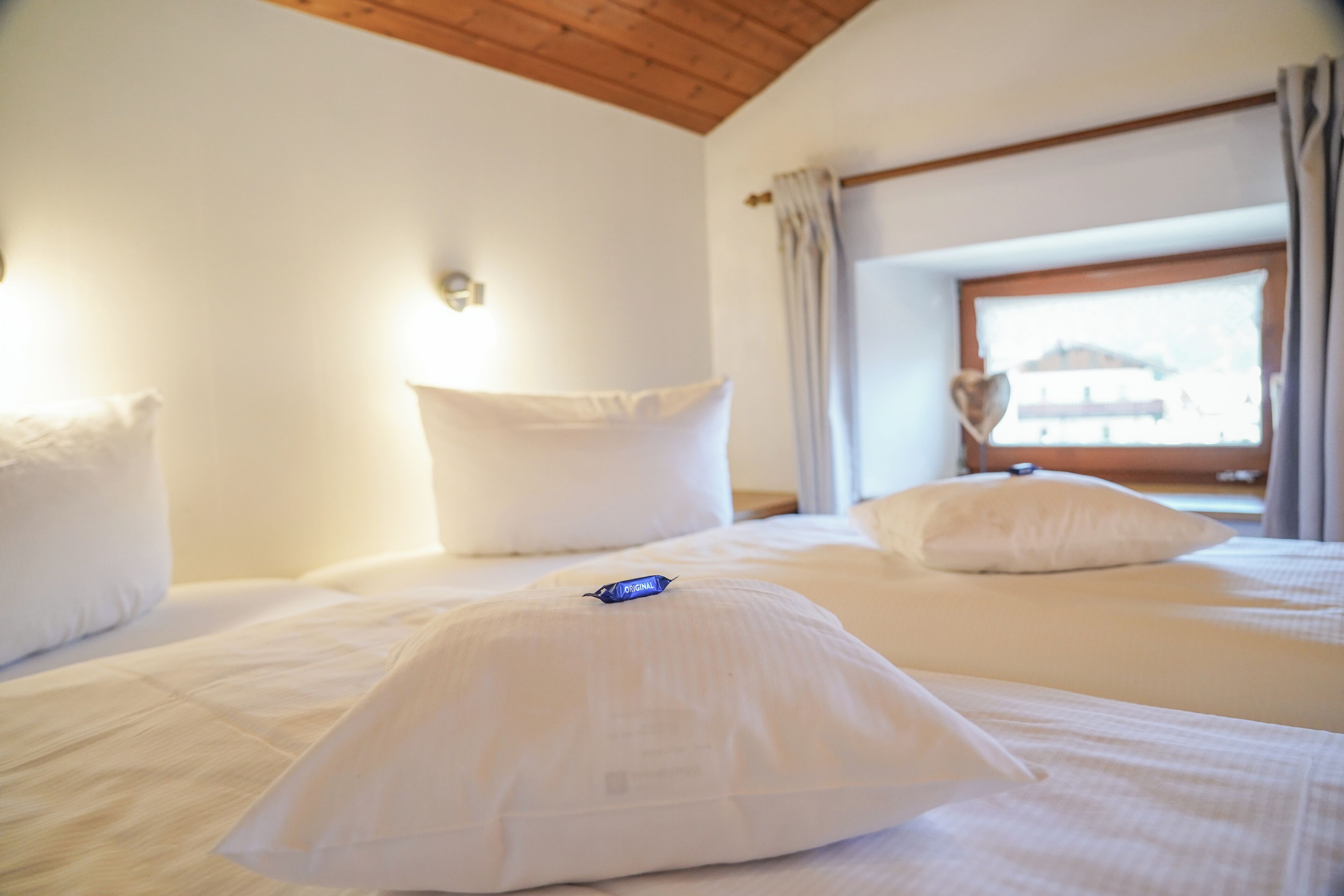 A hotel room with two beds, white bedding, a wooden ceiling, and a window with curtains.